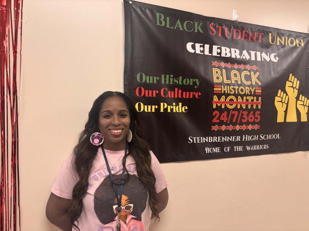 Ms. Thybulle, Sponsor of the Black Student Union (BSU) posing in front of the Black History Month poster hung outside her classroom for all to see. Black History Month has been celebrated by the Black Student Union at Steinbrenner for many years. Photo Courtesy Ademy Malave.  