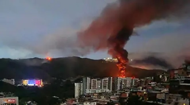 A massive fire burns on a hillside above a residential area, sending thick smoke into the evening sky as crews work to have the flames. Officials said several buildings were threatened as residents watched from nearby high-rises. Photo courtesy of Getty Images.