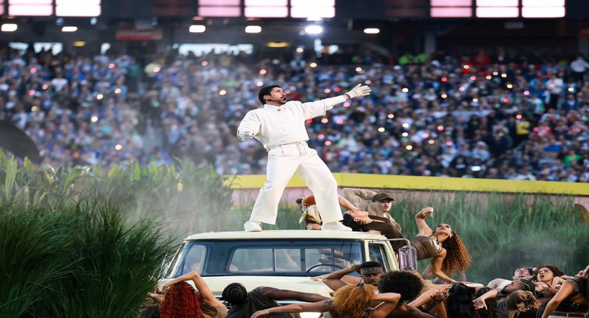 Puerto Rican superstar Bad Bunny stands on top of a vehicle in the center of a packed stadium, pointing out toward the crowd as dancers and stage effects swirl around him. Fans held up glowing phones that created a sea of lights in the stands, capturing the high-energy moment from his live performance. Photo courtesy of The New Yorker